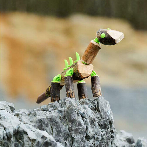 Een zelfgemaakte Brachiosaurus dinosaurus van takken en groene connectors staat op een rots.