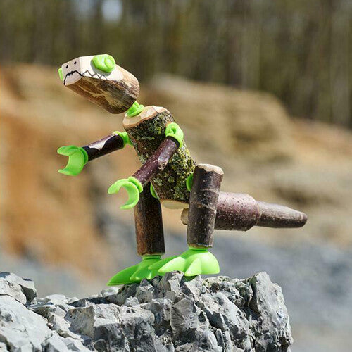 Een zelfgemaakte T-Rex dinosaurus van takken en groene connectors staat op een rots.