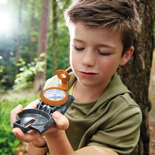 Een kind bekijkt het opengeklapte Haba Terra Kids handkompas in een bosrijke omgeving.