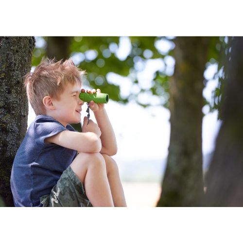 Een jongen zit in een boom en kijkt door de groene Haba Terra Kids monoculair.