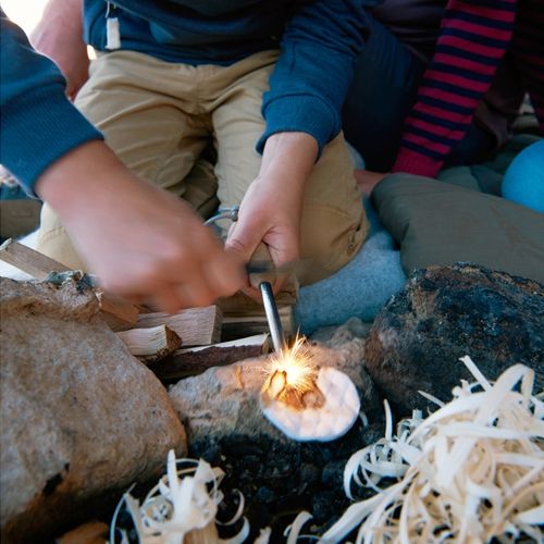 Een kind gebruikt de Haba Terra Kids vuurstarter om een katoenen pad te ontsteken voor een kampvuur.