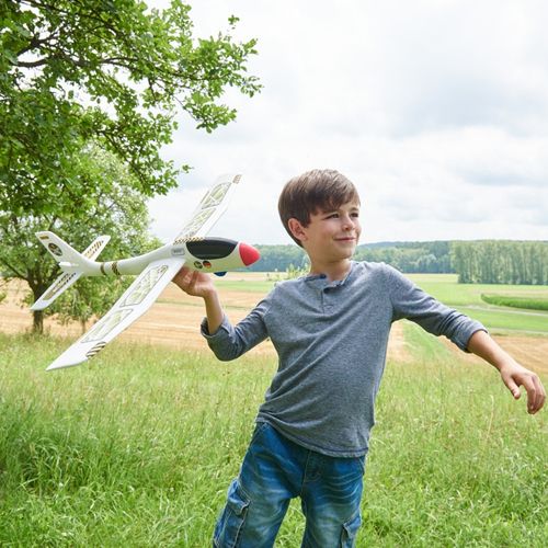 Een lachende jongen houdt het Haba Terra Kids werpvliegtuig maxi vast in een groen veld.