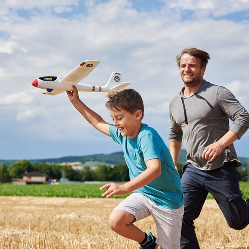 Een jongen en een man rennen lachend in een veld, terwijl de jongen het Haba Terra Kids werpvliegtuig maxi omhoog houdt.