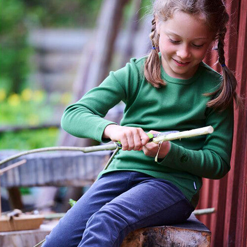 Een kind gebruikt het groene Haba Terra Kids zakmes om een tak te snijden.