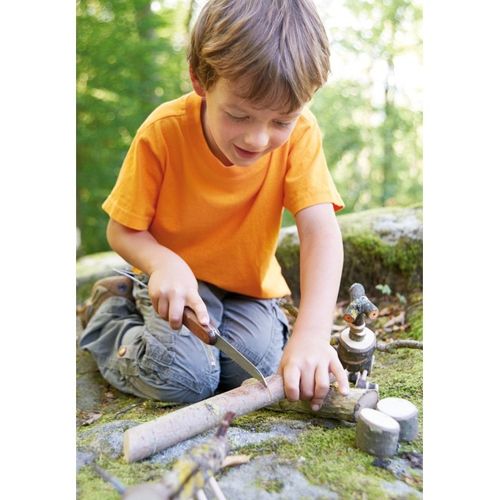 Een kind gebruikt de Haba Terra Kids zakzaag om een tak te zagen in een bosrijke omgeving.