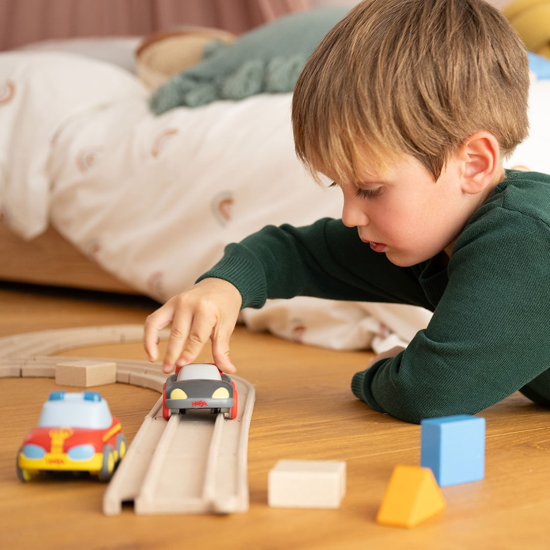 Een jongen speelt op de houten vloer met een rode auto op de Haba Cars speelgoedracebaan.