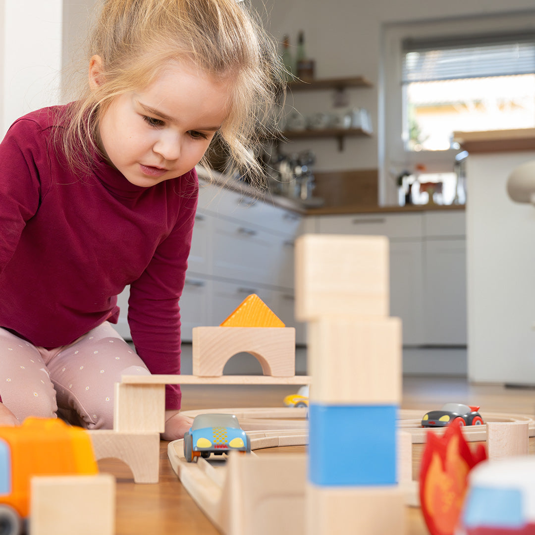 Een meisje speelt geconcentreerd met de Haba Cars autobaan en houten blokken.