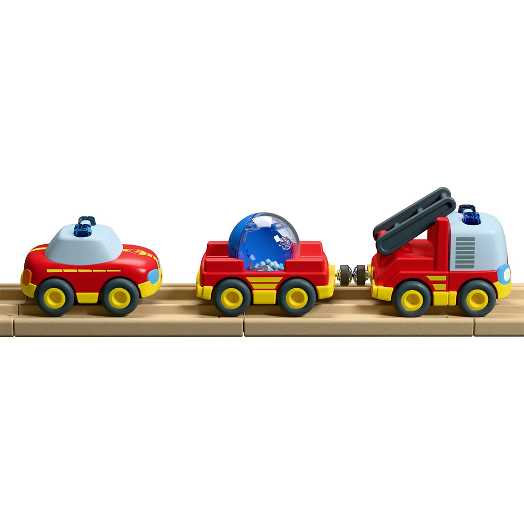 De drie HABA speelgoedauto's van de brandweerset staan op een rij op een houten baan.