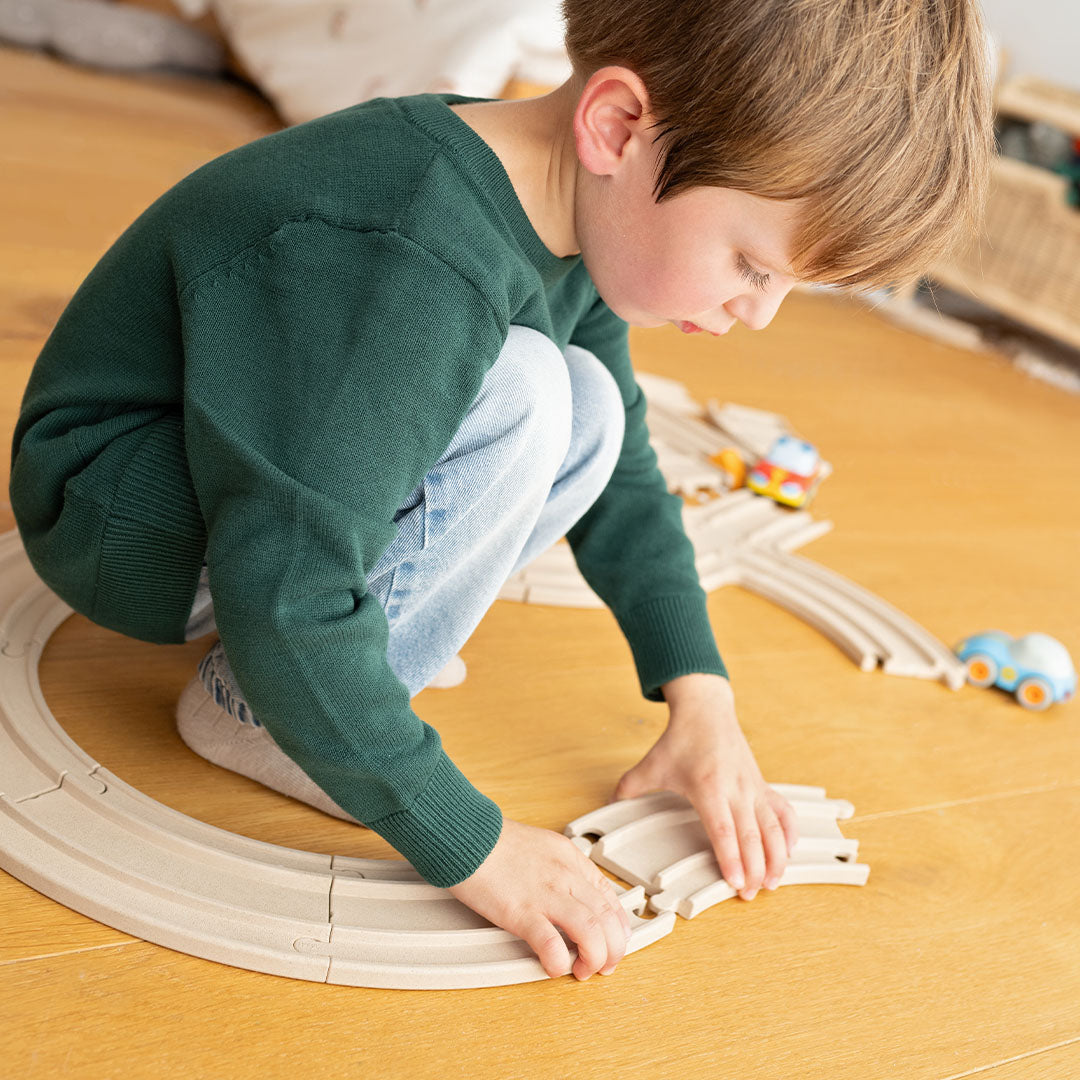 Een kind van ongeveer 4 jaar oud bouwt een racebaan met de houten Haba Cars uitbreidingsset.
