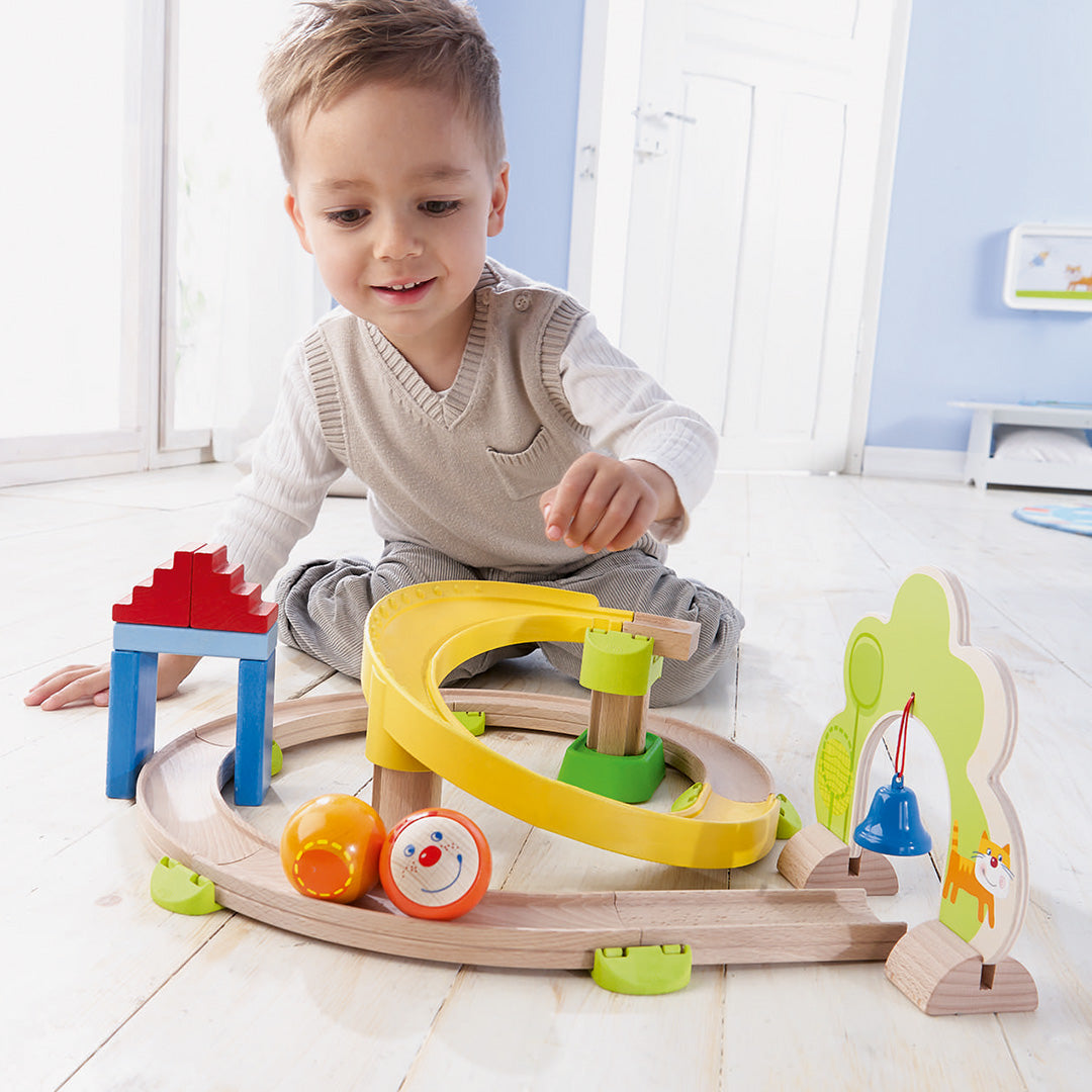 Een lachende jongen speelt met de HABA Kullerbü knikkerbaan met twee ballen en een bel.