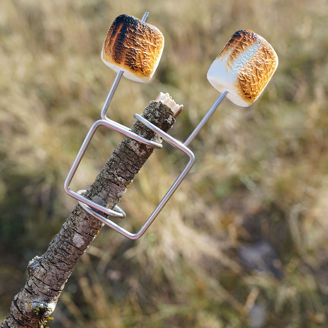 Het zilverkleurige grillspies opzetstuk met twee geroosterde marshmallows op een houten stok.