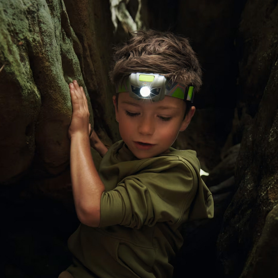 Een jongen met een brandende Haba Terra Kids hoofdlamp op zijn hoofd klimt tussen donkere rotsen.