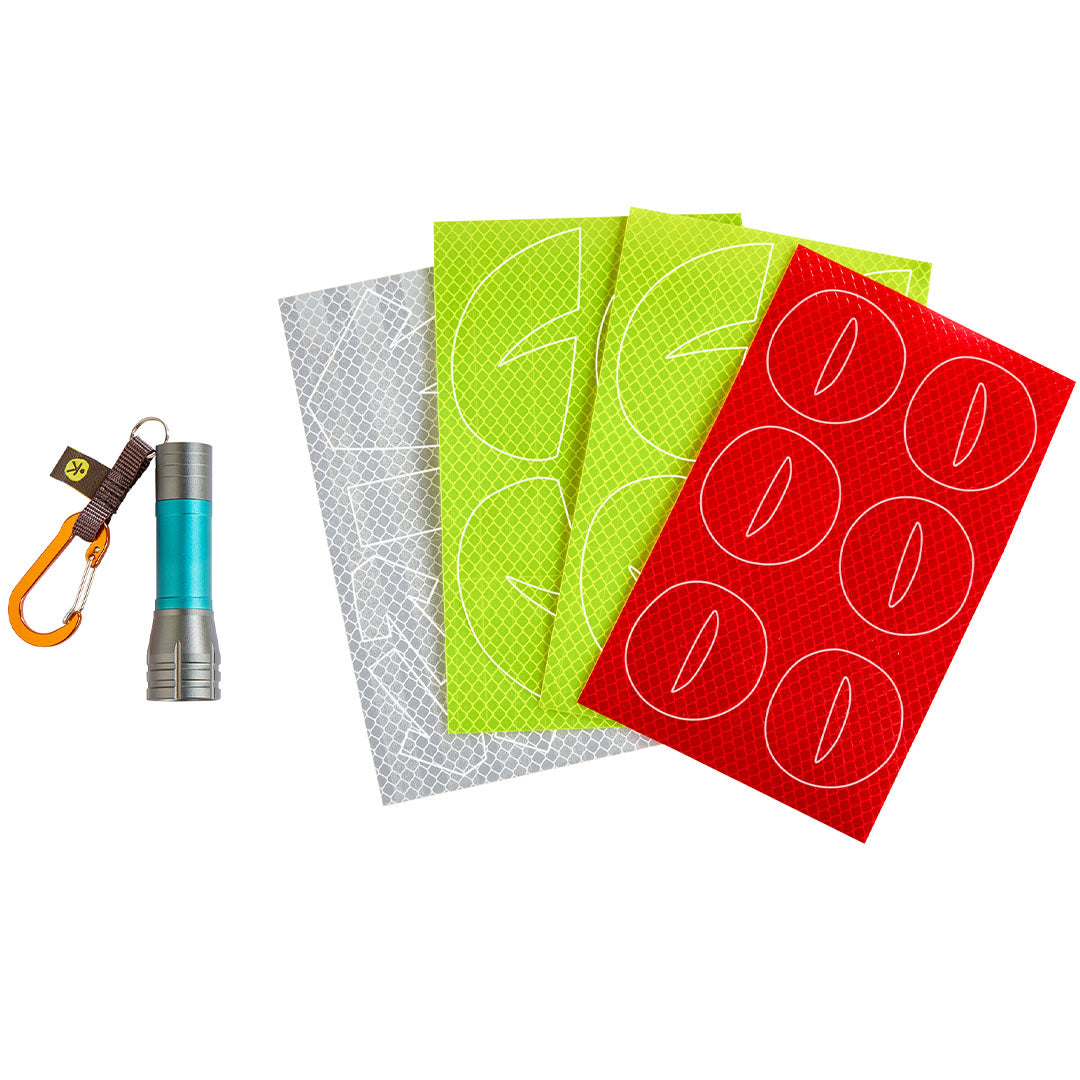 De inhoud van de haba Terra Kids set: een mini zaklamp met karabijnhaak en vier vellen reflecterende stickers in grijs, groen en rood.