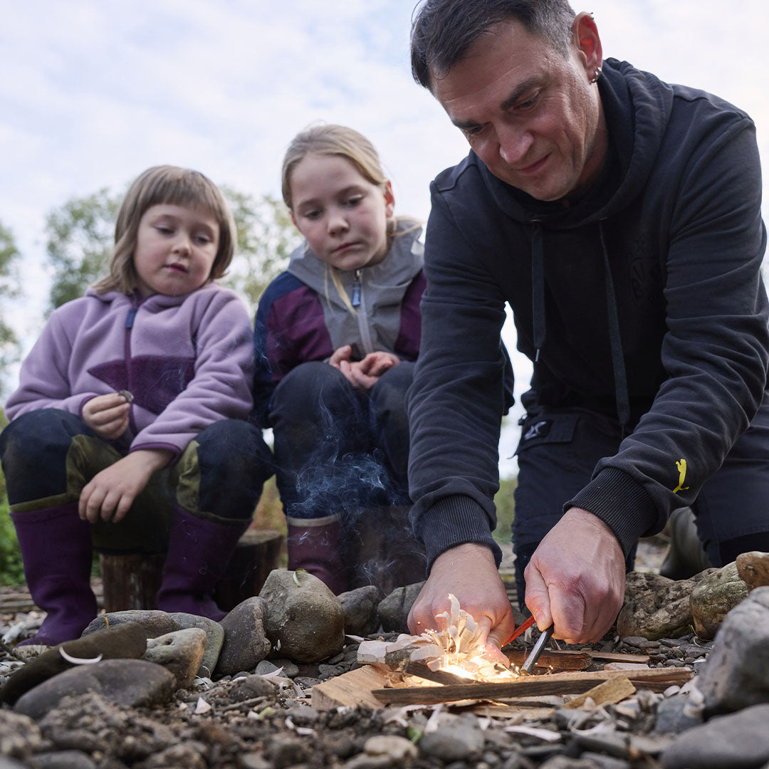 Een volwassene en twee kinderen maken buiten vuur met de Haba Terra Kids vuurstarter.