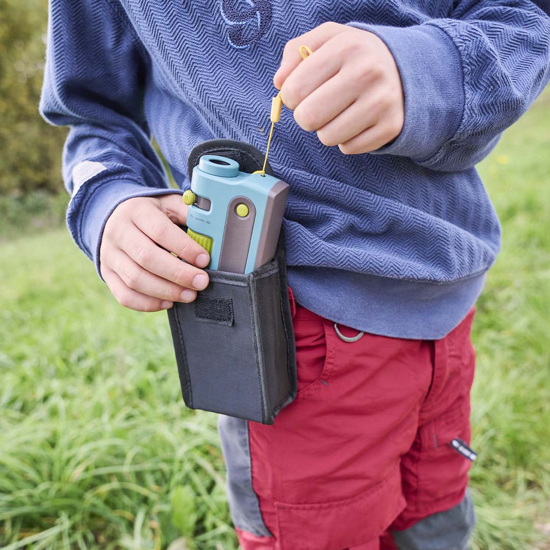 Een kind stopt de Haba Terra Kids zakmicroscoop in een zwart heuptasje.