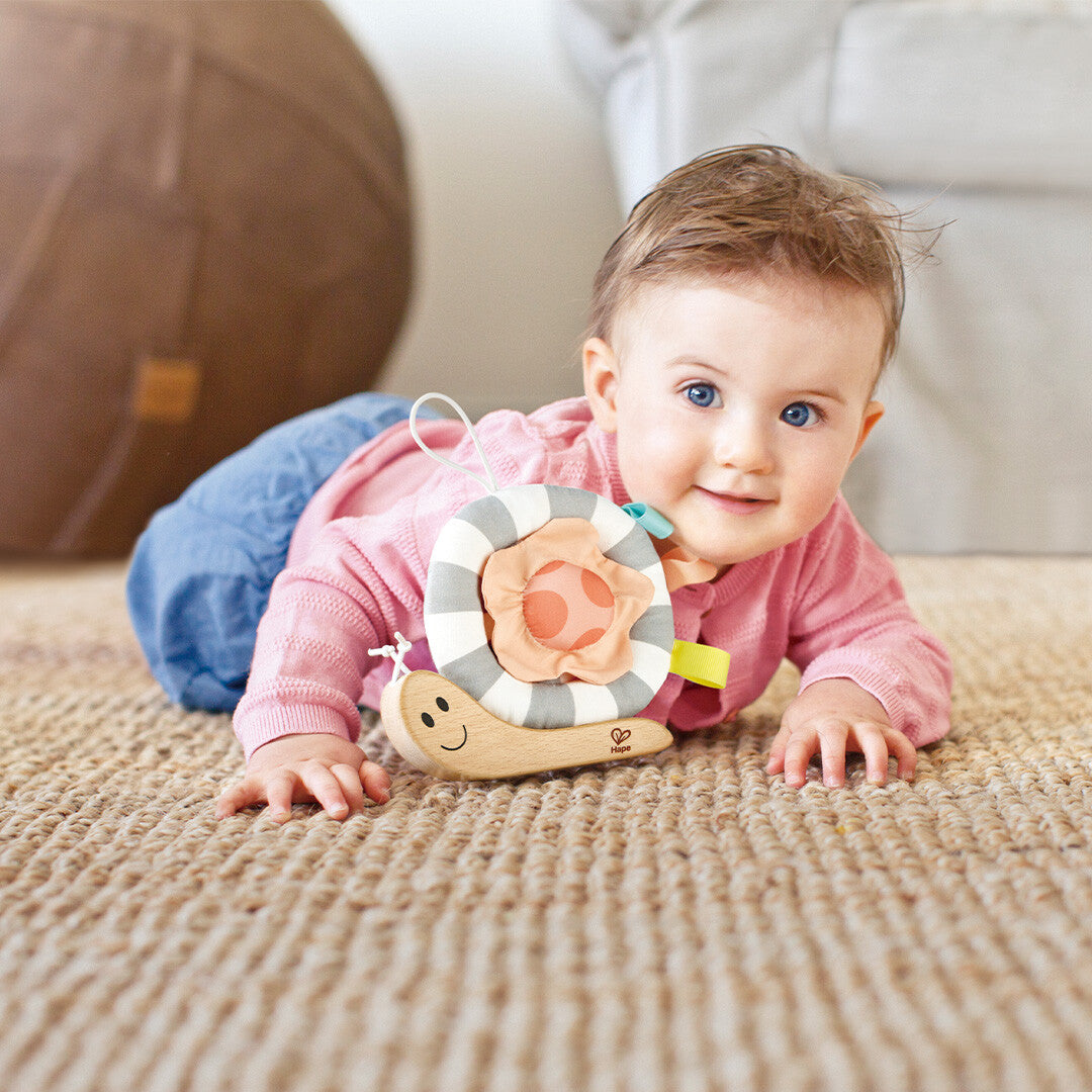 Een lachende baby speelt op de buik met het Hape activiteitenspeeltje slak.