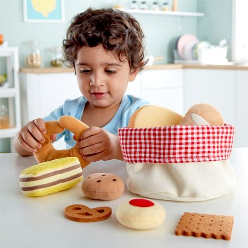 Een kleuter speelt met het Hape stoffen speelgoedbroodmandje en houdt een stoffen krakeling vast.
