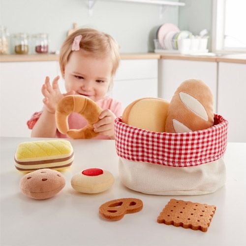 Een kleuter speelt met het Hape stoffen speelgoedbroodmandje en houdt een stoffen croissant vast.