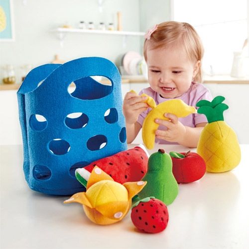 Een lachend kind speelt met het Hape vilten fruitmandje en de fruitstukken, waaronder een banaan.