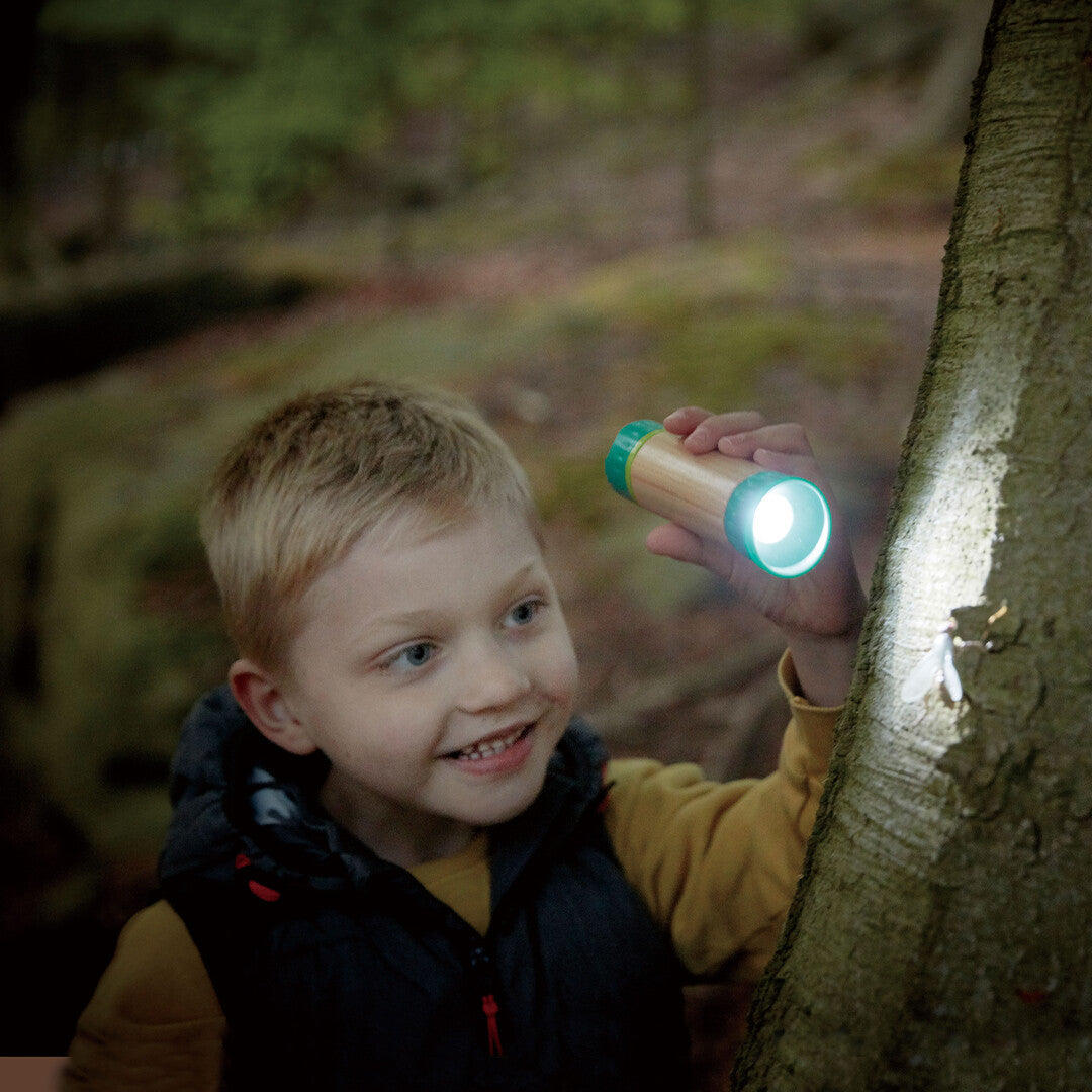 Een jongen schijnt met een zaklamp op een boomstam in het bos.