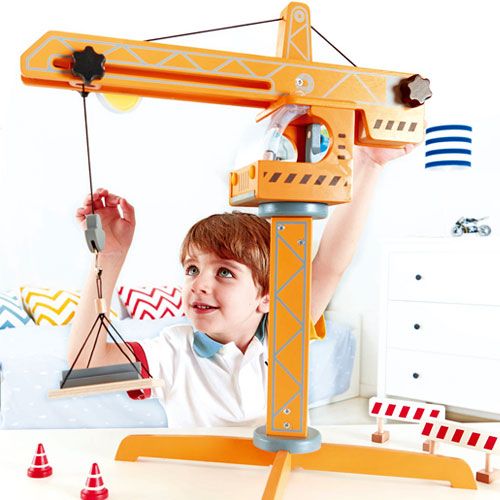 Een jongen speelt met de Hape houten hijskraan die een lading blokken omhoog hijst.