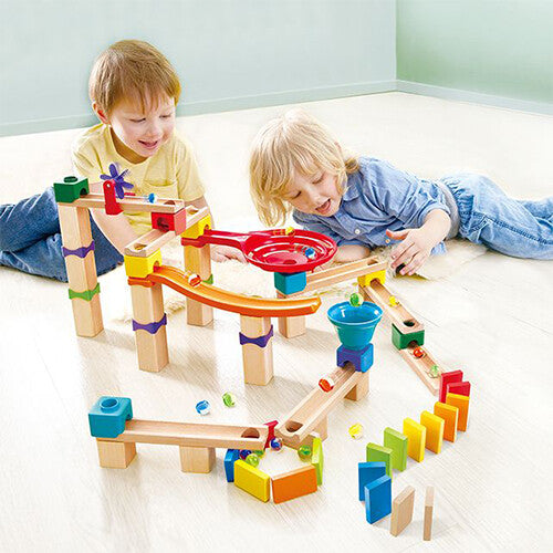 Twee kinderen spelen op de vloer met de Hape knikkerbaan rally set.