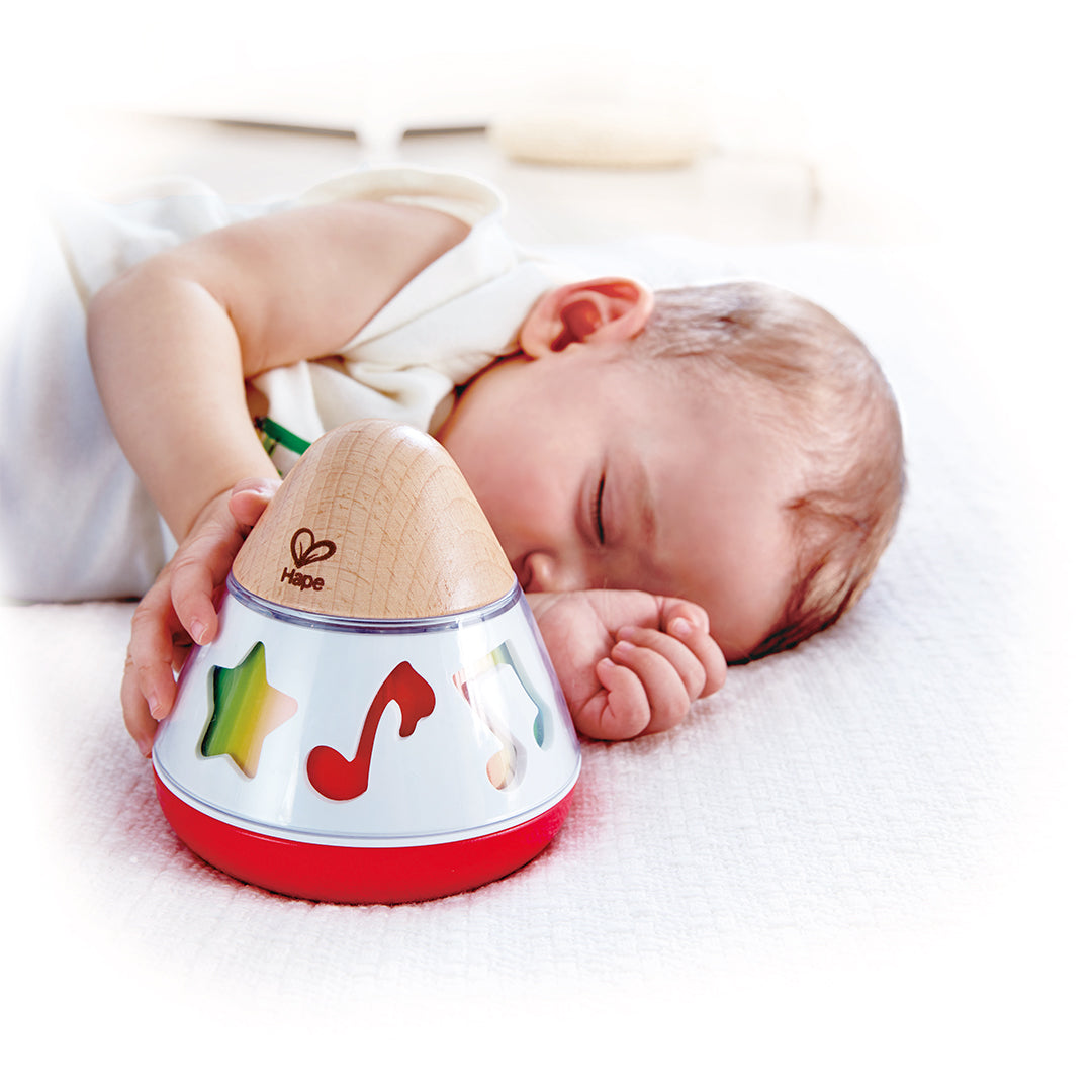 Een slapende baby ligt naast het Hape muziekspeelgoed met ster- en muzieknootuitsparingen.