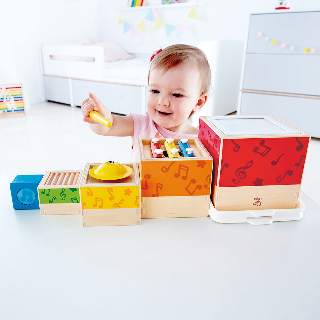 Een lachende baby speelt met de Hape muzikale bouwblokken voor baby's, die horizontaal op een tafel liggen.