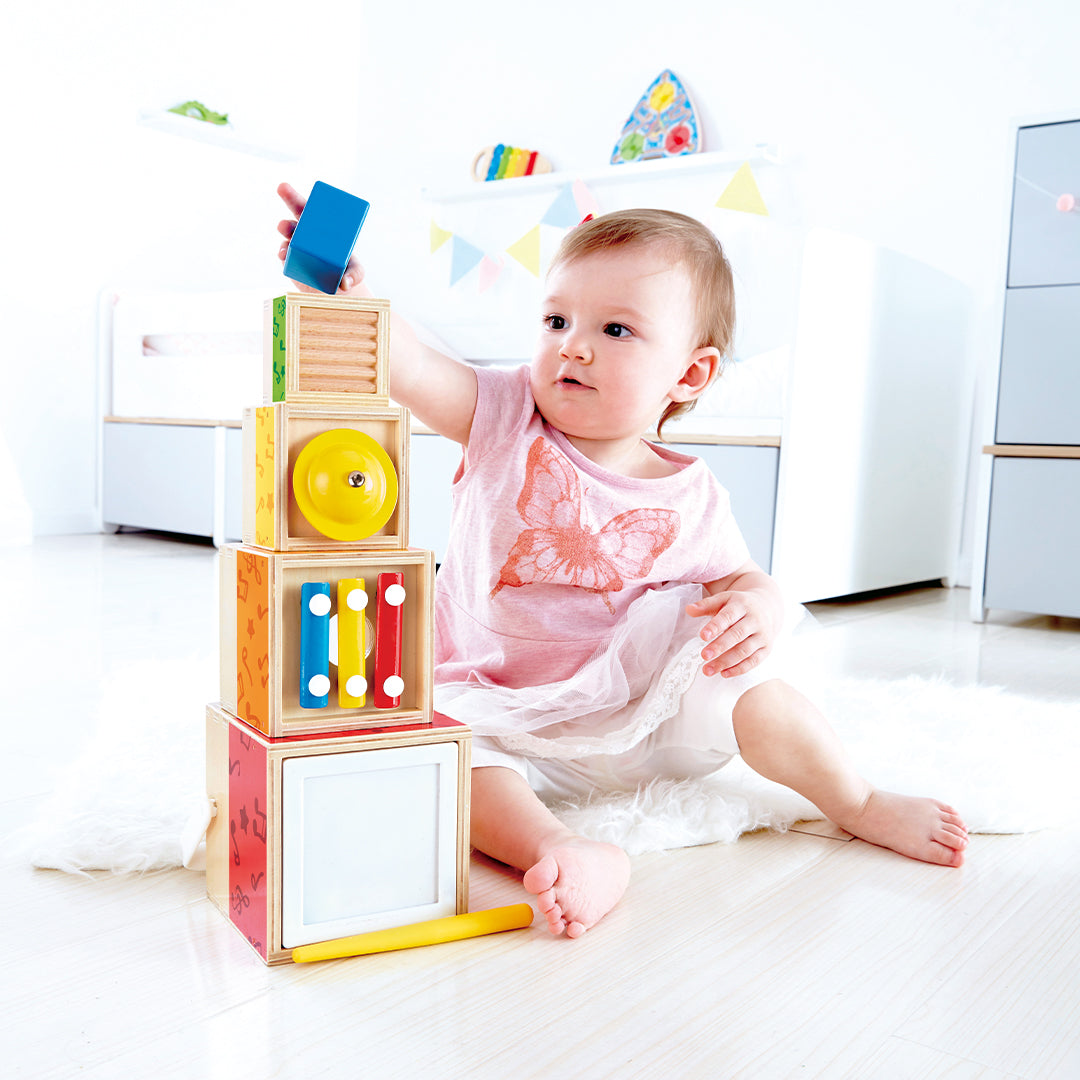 Een baby zit op de grond en stapelt de Hape muzikale bouwblokken voor baby's tot een toren.