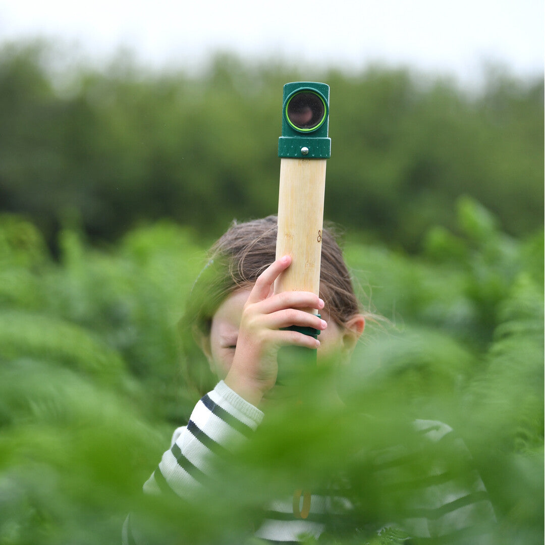 Een kind kijkt door de periscoop, deels verborgen in groen gebladerte.