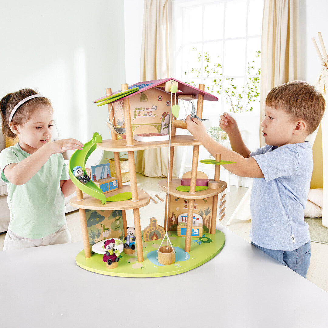 Twee kinderen spelen samen met het Hape houten poppenhuis in boomhutstijl met pandafamiliefiguren.