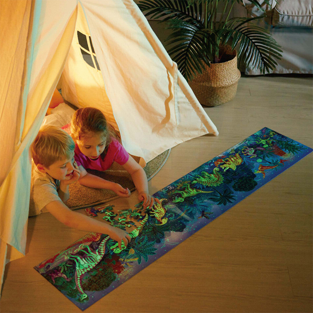 Twee kinderen kijken in een tent naar de oplichtende Hape dinosaurus legpuzzel op de vloer.