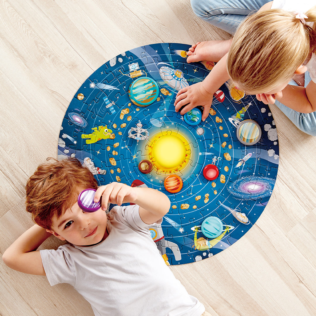 Een jongen en een meisje spelen met de Hape zonnestelsel legpuzzel op de houten vloer.