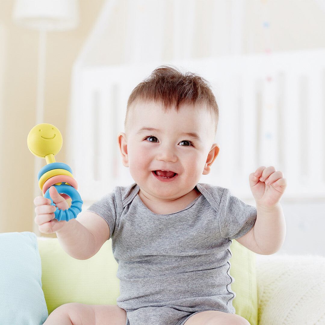 Een lachende baby speelt met de Hape rammelaar met gele smiley.