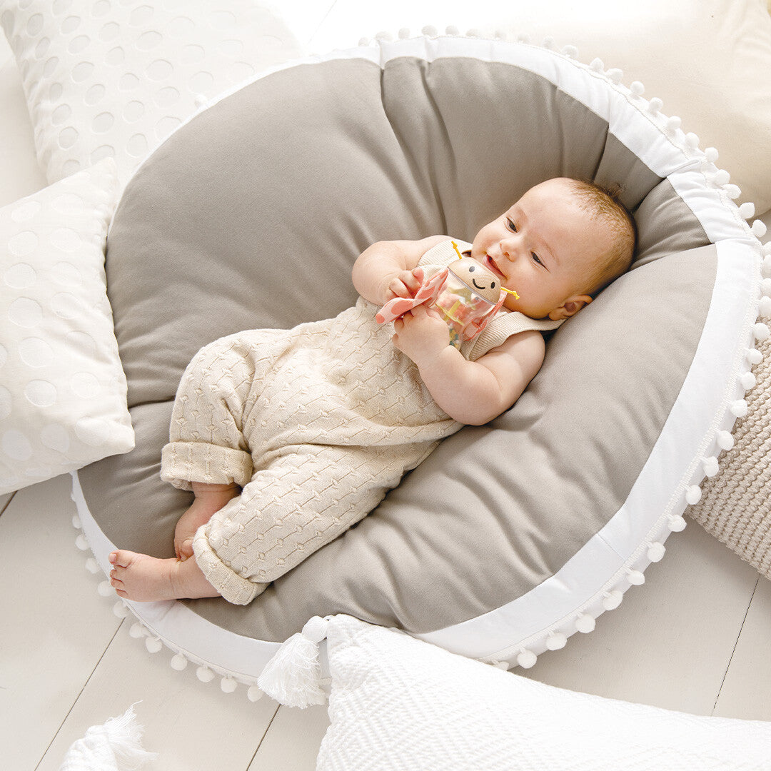 Een baby ligt op een grijze speelmat en speelt met de Hape vlinder rammelaar.