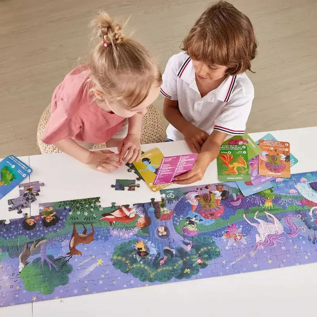 Twee kinderen leggen de Hape 'Magic Forest' vloerpuzzel met fantasiefiguren en dieren op een witte tafel.