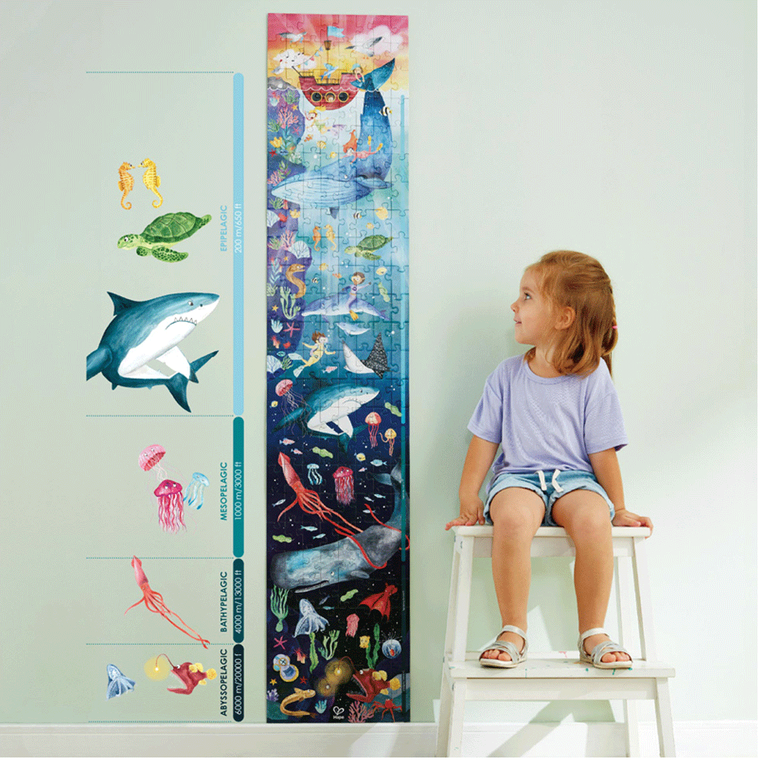 Een meisje zit naast de Hape oceaan vloerpuzzel die als diepteschaal met zeedieren tegen de muur staat.