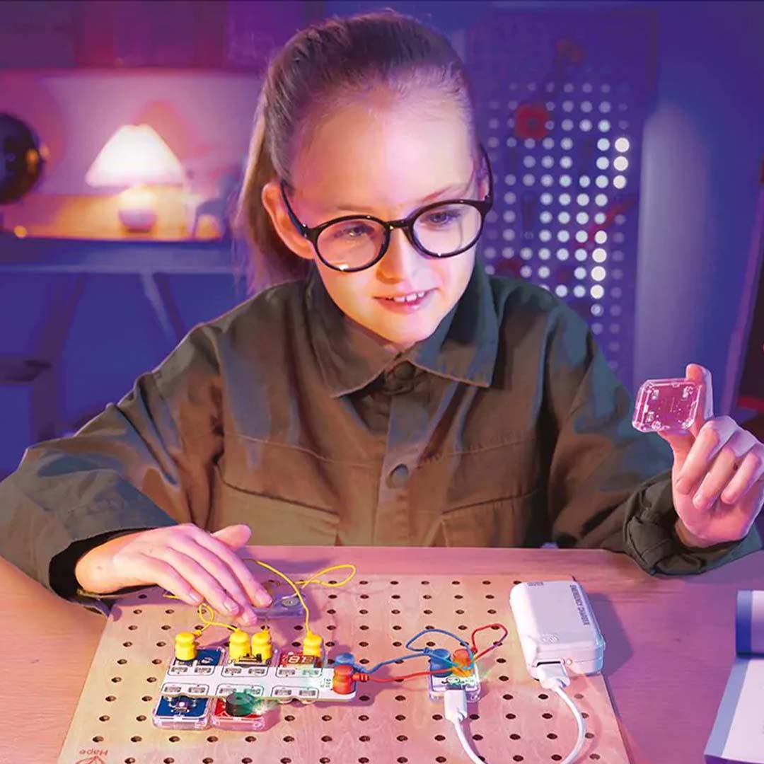 Een meisje met bril bouwt een circuit op de Hape Lab Box Circuit Explorer Pro.