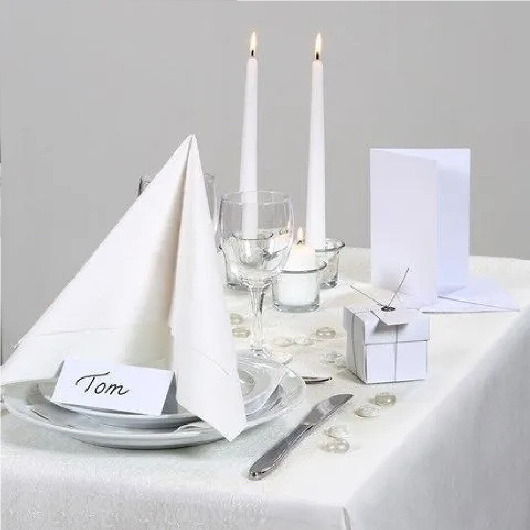 Een feestelijk gedekte tafel met witte servetten, kaarsen en een naamkaartje.