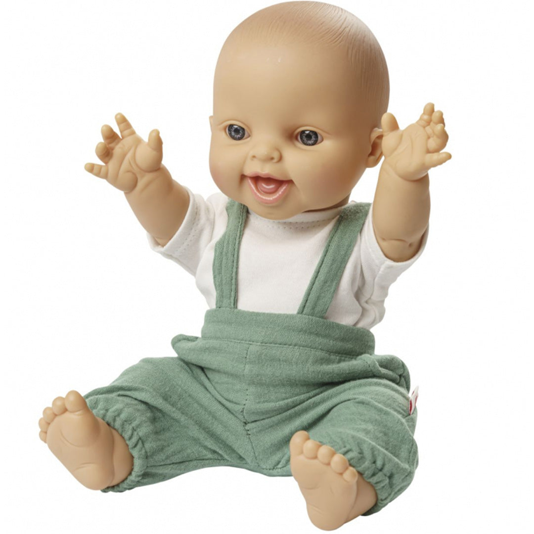 Een baby pop draagt de saliegroene tuinbroek en het witte t-shirt, zittend met opgeheven armen.