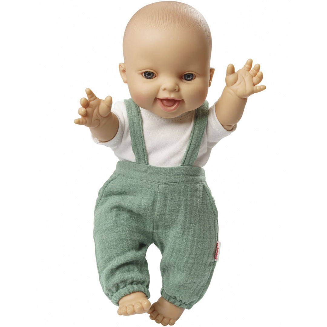Een baby pop draagt de saliegroene tuinbroek en het witte t-shirt, staand met opgeheven armen.