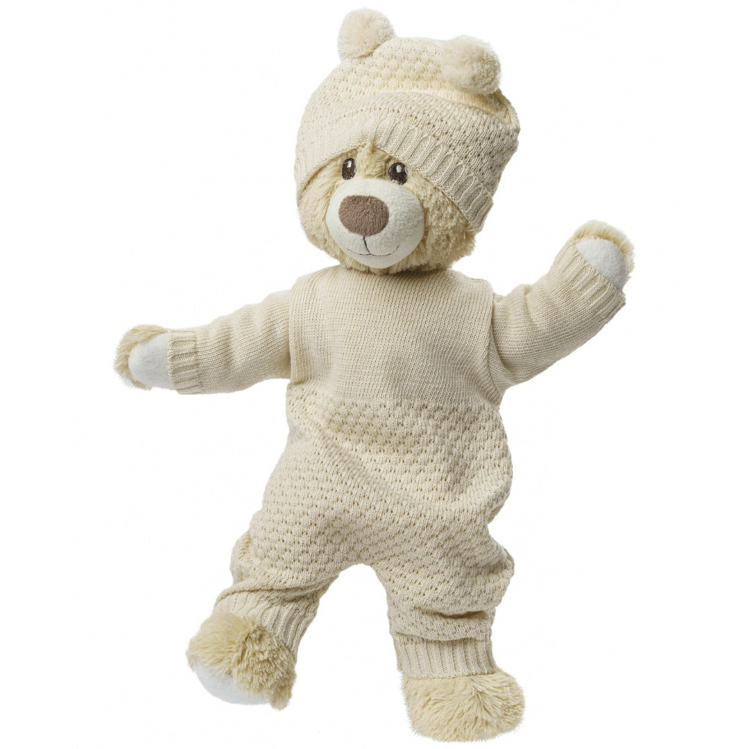 Een teddybeer draagt de heless gebreide beige poppenmuts met pompons en een bijpassend gebreid pakje.