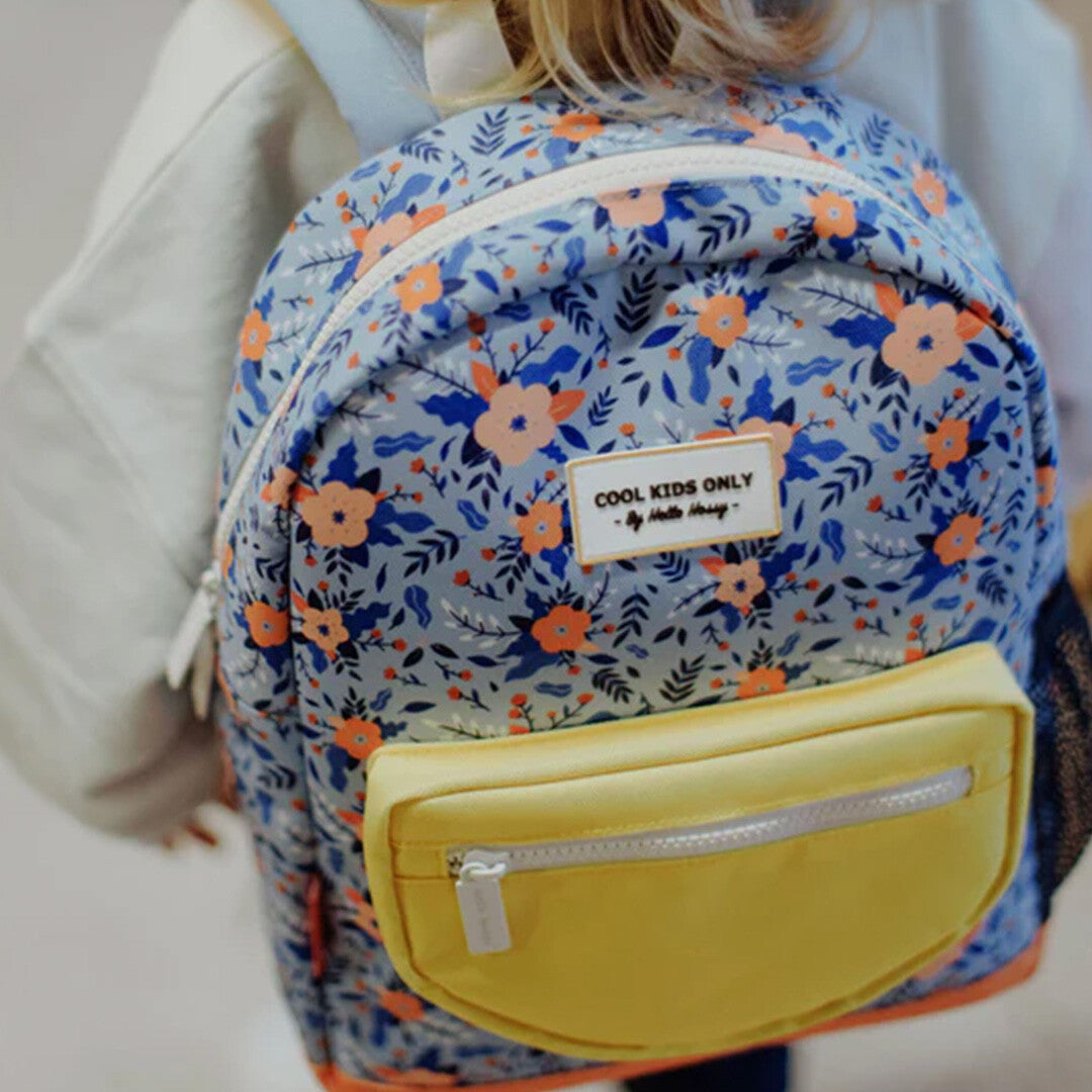 Een kind draagt de Hello Hossy kleuterrugzak met blauw gebloemd patroon en gele voorzak, van achteren gezien.