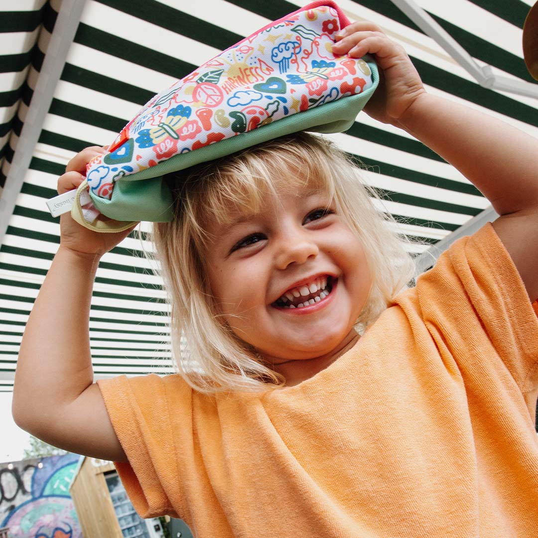 Een lachend kind met blond haar houdt het hello hossy pennenetui op haar hoofd.