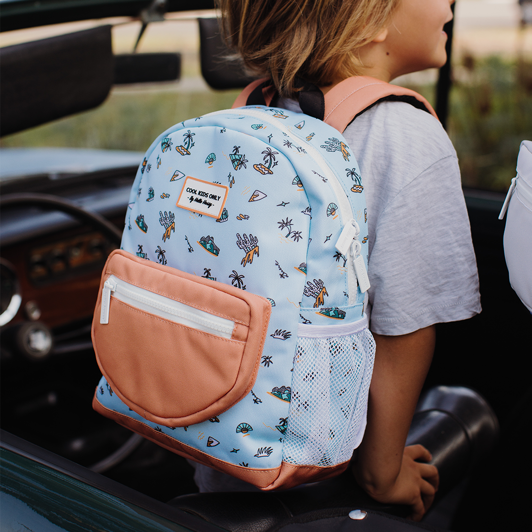 Kind draagt de hello hossy schoolrugzak met blauw eilandpatroon in een auto.