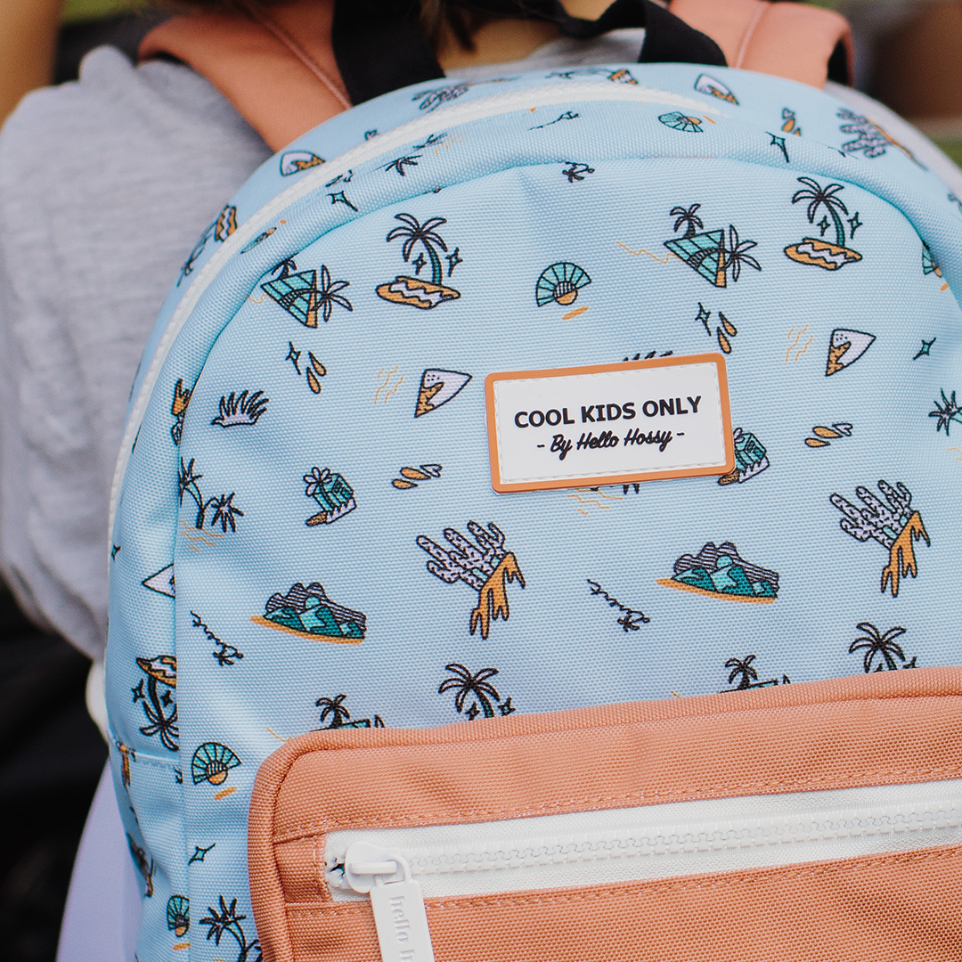Close-up van de hello hossy schoolrugzak met het 'COOL KIDS ONLY' label en het blauwe eilandpatroon.