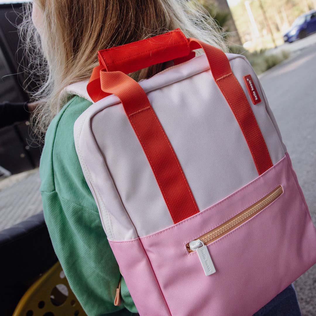 Een kind draagt de hello hossy schoolrugzak in roze en oranje op de rug, gezien van achteren.