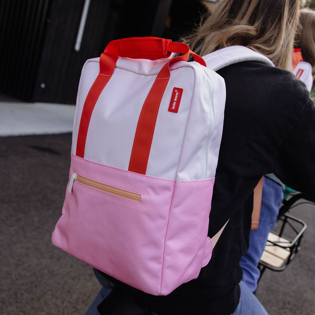 Een persoon draagt de hello hossy schoolrugzak in roze en oranje op de rug tijdens het fietsen.