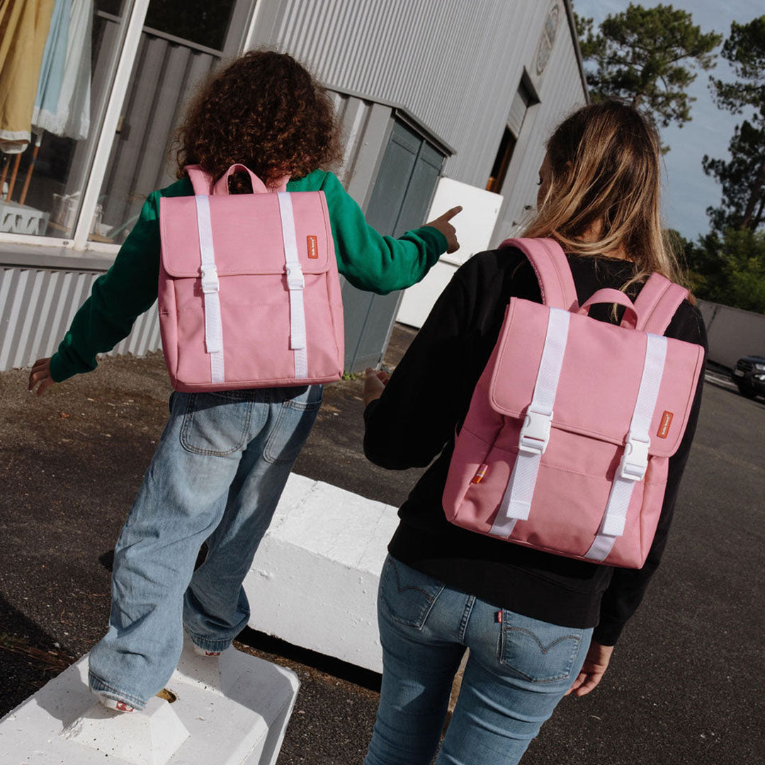 Een kind en een volwassene dragen de hello hossy roze schoolrugzakken buiten.