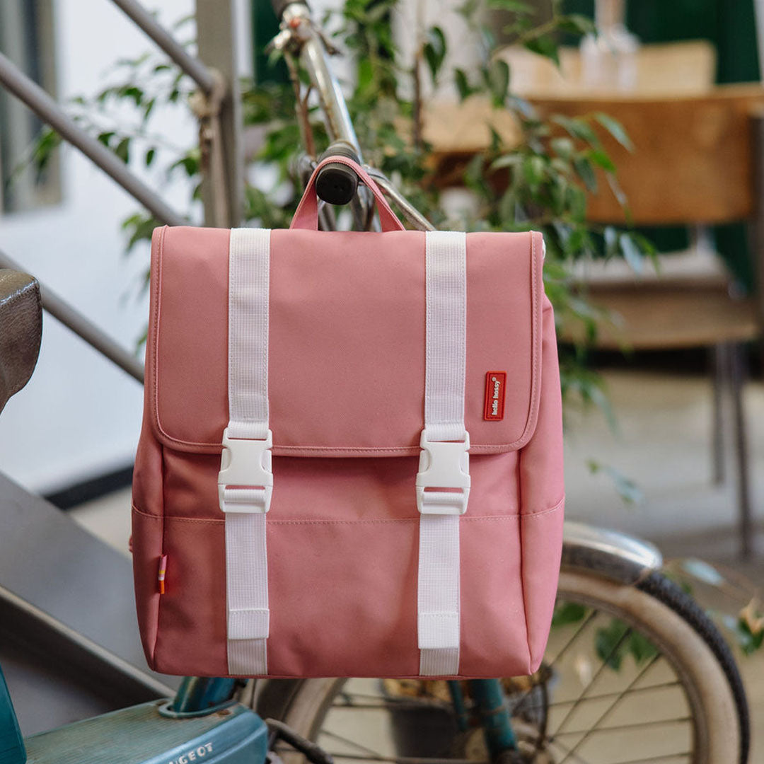 De hello hossy roze schoolrugzak hangt aan het stuur van een fiets.